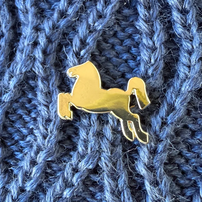 Goldener Ansteckpin in Form eines Rosses, der an blauem Strick-Stoff pinnt